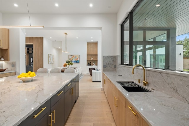 kitchen with light stone countertops, light wood-type flooring, tasteful backsplash, sink, and decorative light fixtures