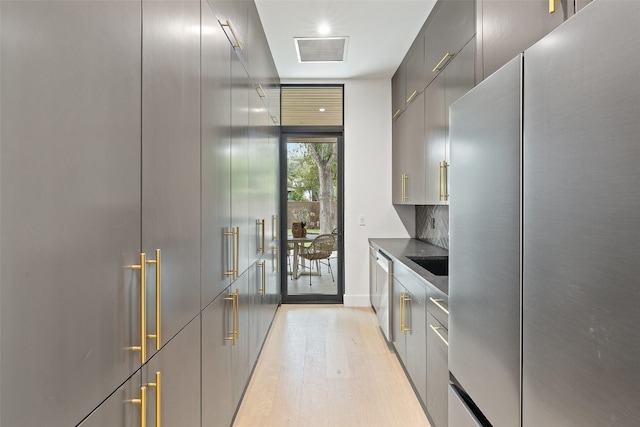 kitchen with tasteful backsplash, gray cabinets, stainless steel appliances, and light wood-type flooring