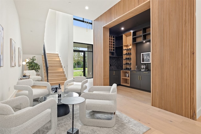 living room with a high ceiling, light hardwood / wood-style floors, and bar