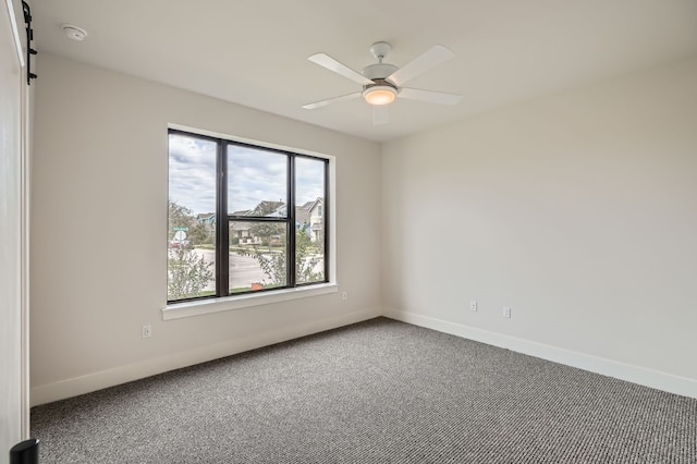 carpeted spare room with a barn door and ceiling fan