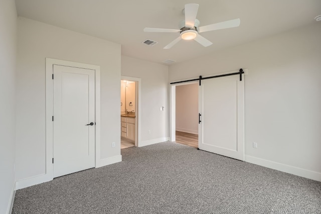 unfurnished bedroom featuring a barn door, ceiling fan, connected bathroom, and carpet floors