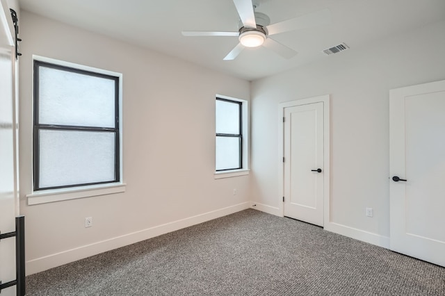 unfurnished bedroom with carpet flooring, a barn door, and ceiling fan