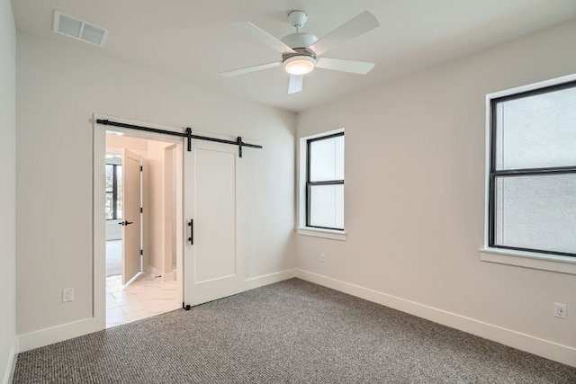 unfurnished bedroom featuring multiple windows, a barn door, and ceiling fan