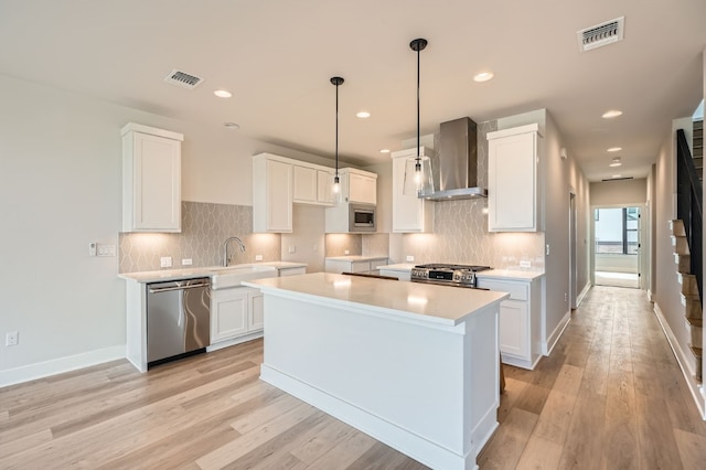 kitchen with stainless steel appliances, wall chimney range hood, a kitchen island, white cabinetry, and light wood-type flooring