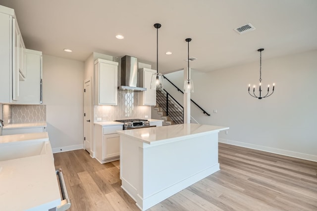 kitchen featuring white cabinets, wall chimney range hood, light wood-type flooring, and hanging light fixtures