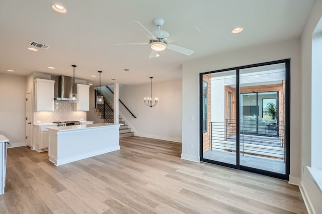 kitchen with light wood-type flooring, wall chimney range hood, hanging light fixtures, and white cabinets