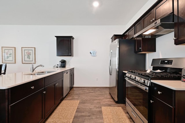 kitchen featuring stainless steel appliances, a sink, under cabinet range hood, wood finished floors, and a peninsula