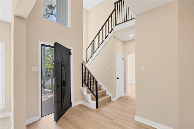 entrance foyer with a towering ceiling, light wood finished floors, baseboards, and stairway