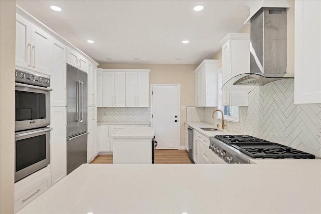 kitchen featuring wall chimney exhaust hood, appliances with stainless steel finishes, light countertops, and white cabinets