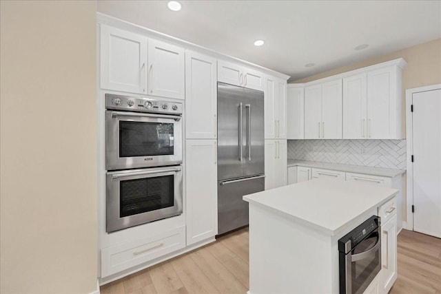 kitchen featuring stainless steel appliances, white cabinetry, light countertops, backsplash, and light wood finished floors