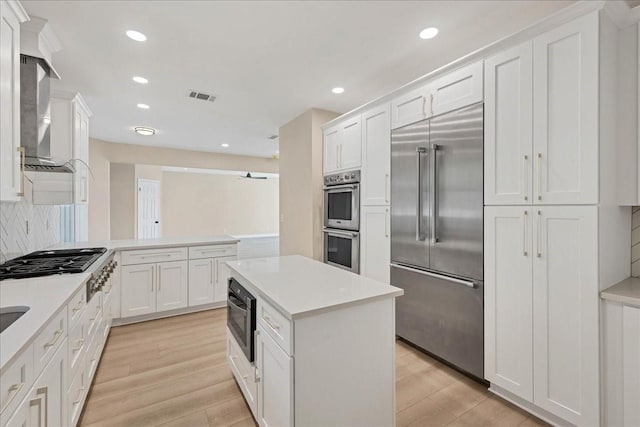 kitchen with built in appliances, white cabinetry, light countertops, decorative backsplash, and light wood finished floors