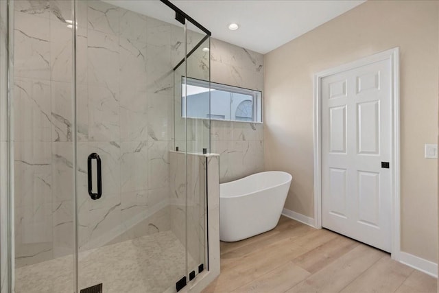 bathroom featuring a freestanding tub, wood finished floors, a marble finish shower, and baseboards