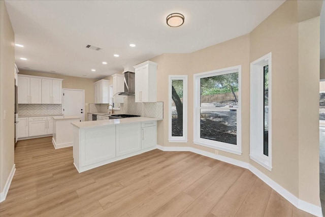 kitchen featuring light countertops, decorative backsplash, white cabinets, wall chimney range hood, and a peninsula