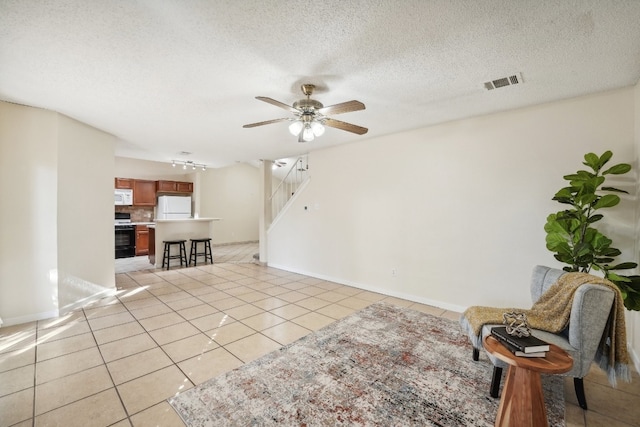 interior space featuring a textured ceiling, light tile patterned floors, and ceiling fan