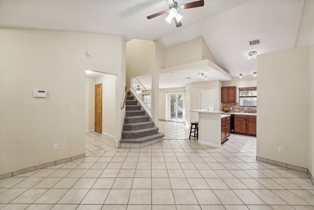 unfurnished living room with ceiling fan, sink, light tile patterned floors, and lofted ceiling