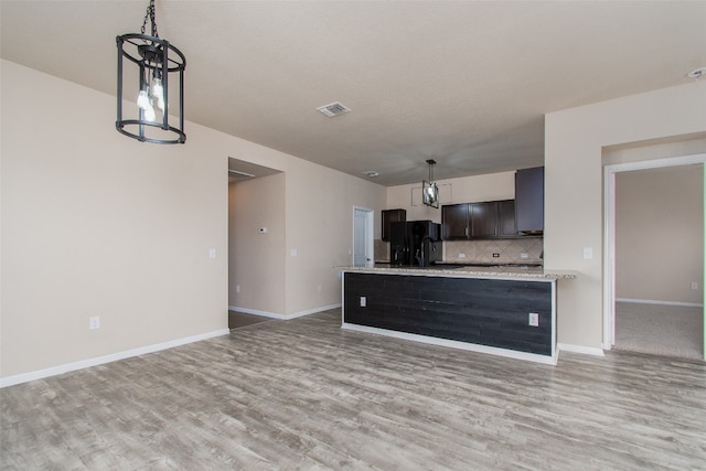 kitchen with tasteful backsplash, black fridge, light hardwood / wood-style flooring, and pendant lighting