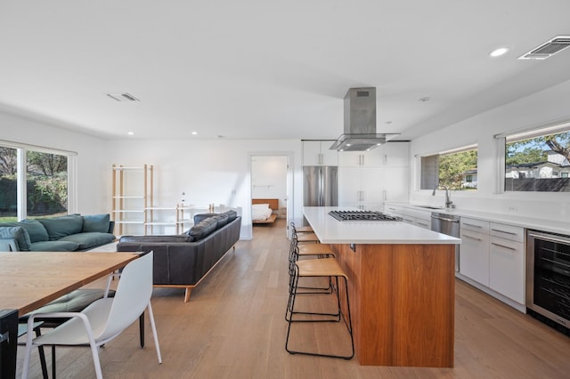 kitchen with wine cooler, ventilation hood, light hardwood / wood-style flooring, a kitchen island, and white cabinets