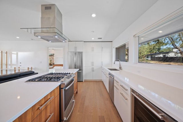 kitchen featuring white cabinetry, sink, appliances with stainless steel finishes, wall chimney exhaust hood, and light hardwood / wood-style flooring