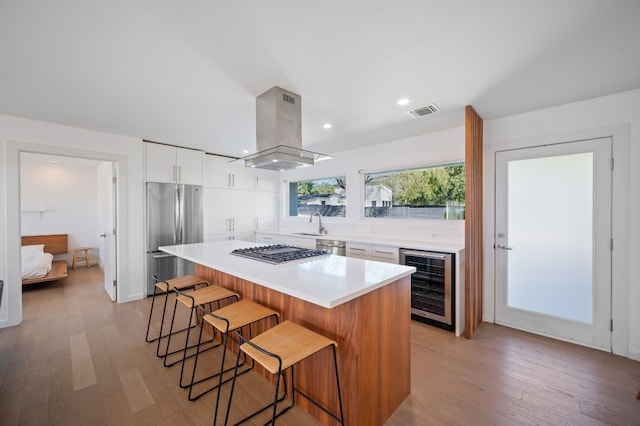 kitchen featuring a center island, beverage cooler, white cabinets, island exhaust hood, and appliances with stainless steel finishes