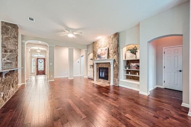 unfurnished living room featuring ceiling fan, dark wood-type flooring, built in features, decorative columns, and a fireplace