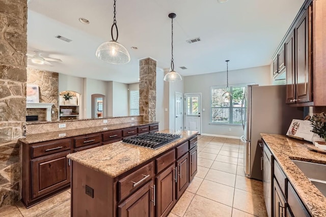 kitchen featuring light stone counters, dark brown cabinets, stainless steel appliances, a kitchen island, and hanging light fixtures