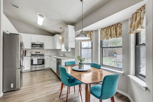 kitchen featuring stainless steel appliances, white cabinetry, hanging light fixtures, vaulted ceiling, and light hardwood / wood-style flooring