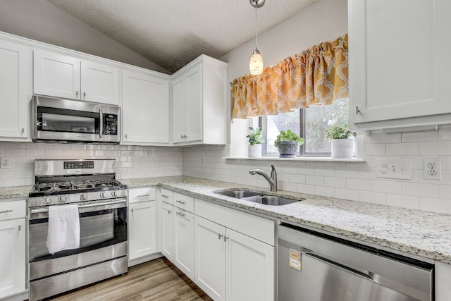 kitchen featuring stainless steel appliances, backsplash, white cabinetry, sink, and vaulted ceiling