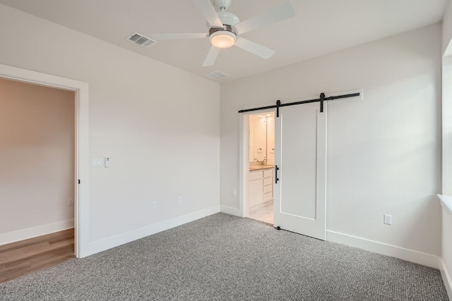 unfurnished bedroom with a barn door, ceiling fan, connected bathroom, and carpet