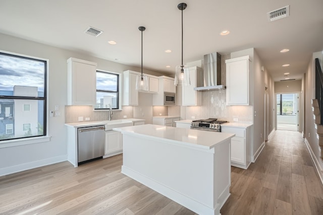 kitchen with white cabinets, stainless steel appliances, and wall chimney range hood