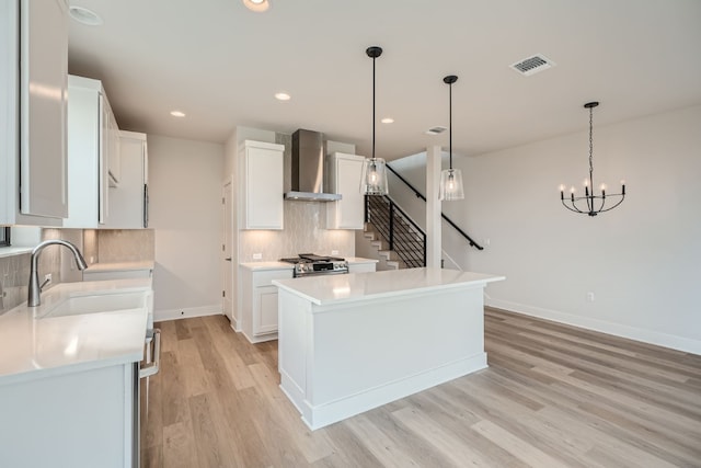 kitchen with white cabinetry, sink, wall chimney exhaust hood, hanging light fixtures, and a kitchen island