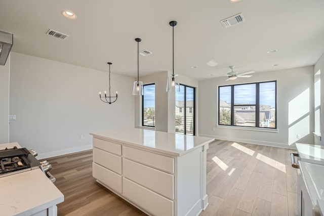 kitchen featuring ceiling fan with notable chandelier, light hardwood / wood-style flooring, a center island, white cabinets, and pendant lighting