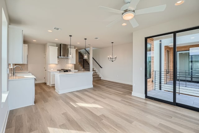 kitchen with light wood-type flooring, wall chimney range hood, decorative light fixtures, decorative backsplash, and white cabinets