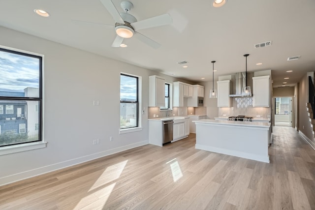 kitchen with white cabinets, wall chimney range hood, a center island, and decorative light fixtures