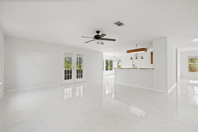 spare room featuring ceiling fan with notable chandelier and french doors