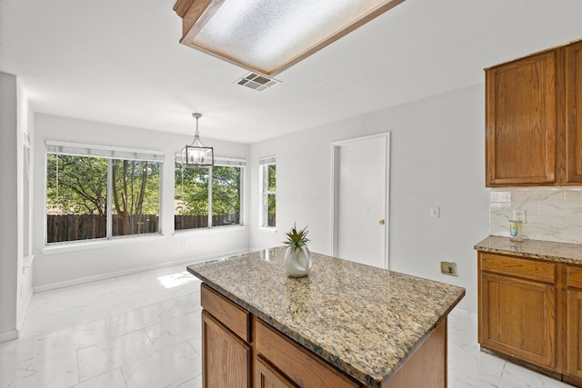 kitchen featuring decorative backsplash, hanging light fixtures, a center island, and light stone countertops