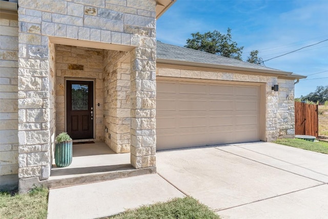 doorway to property featuring stone siding, driveway, and roof with shingles