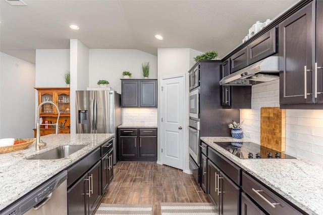 kitchen featuring a sink, under cabinet range hood, appliances with stainless steel finishes, tasteful backsplash, and light stone counters