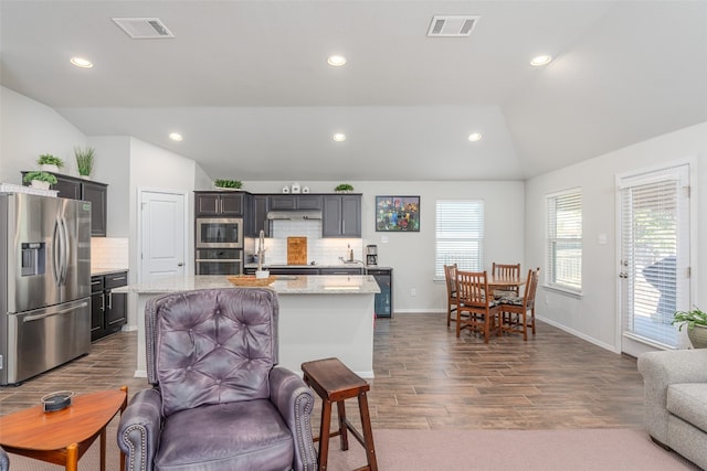 kitchen with a center island with sink, stainless steel appliances, and vaulted ceiling