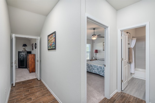 hall with dark colored carpet and vaulted ceiling