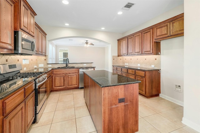 kitchen featuring light tile patterned flooring, sink, appliances with stainless steel finishes, dark stone counters, and a center island