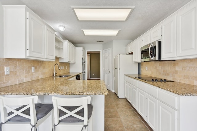 kitchen featuring a kitchen bar, black electric cooktop, white cabinets, kitchen peninsula, and sink