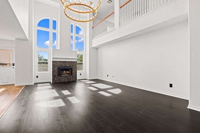 unfurnished living room with a towering ceiling, a stone fireplace, dark hardwood / wood-style flooring, and a notable chandelier