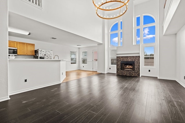 unfurnished living room with a towering ceiling, dark hardwood / wood-style floors, and an inviting chandelier