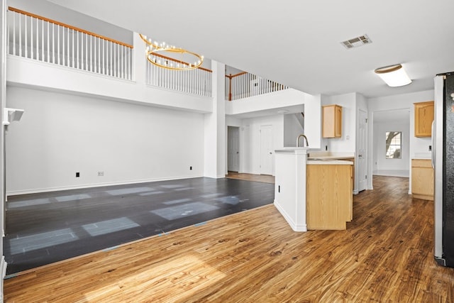 kitchen with a high ceiling, stainless steel refrigerator, light brown cabinets, a chandelier, and dark hardwood / wood-style flooring