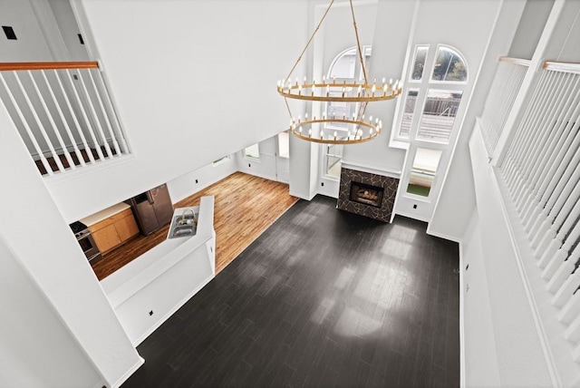 living room with a towering ceiling, dark hardwood / wood-style flooring, a chandelier, and a premium fireplace