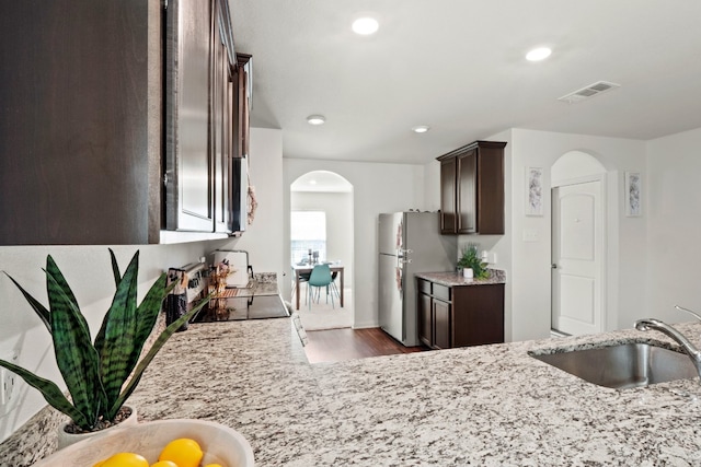 kitchen featuring stainless steel appliances, dark brown cabinetry, light stone countertops, hardwood / wood-style floors, and sink