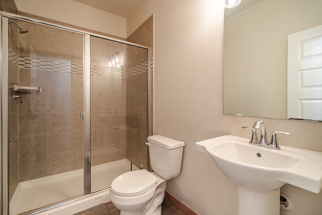 bathroom with toilet, sink, and a shower with shower door