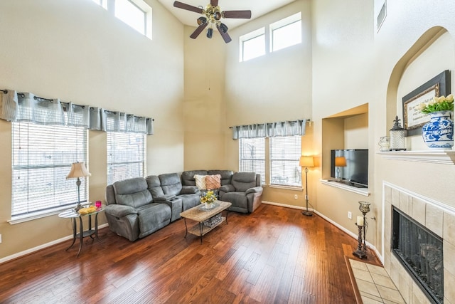 living room with a tiled fireplace, hardwood / wood-style flooring, a high ceiling, and ceiling fan