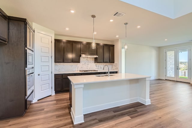 kitchen with light wood-type flooring, a center island with sink, hanging light fixtures, and sink