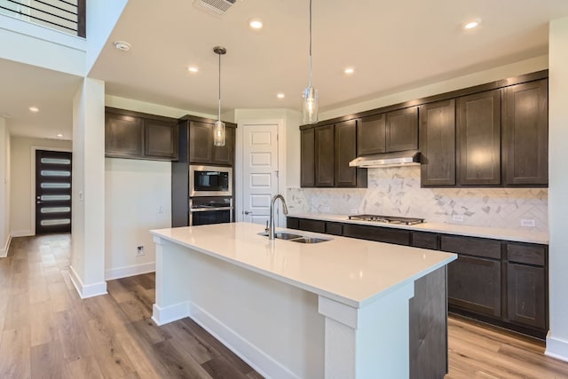 kitchen with hanging light fixtures, stainless steel appliances, light wood-type flooring, and sink